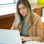 Crop concentrated female freelancer sitting at table and browsing laptop while working online on project