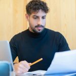 Focused young man reviewing documents at a desk in a modern office setting.