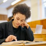 Young woman intently reading a book in a university lecture hall setting.